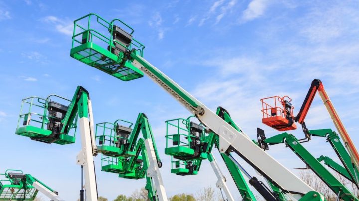 Green, white, and orange aerial lifts are raised under a blue sky with trees in the background, highlighting fleet management.