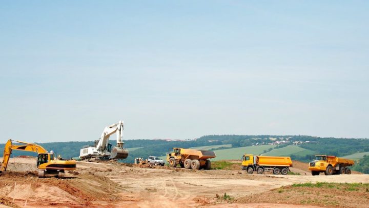 Excavators and dump trucks with a fuel management system work on a dirt site, showcasing construction equipment tracking.