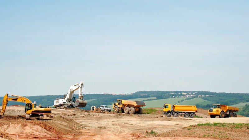 Excavators and dump trucks with a fuel management system work on a dirt site, showcasing construction equipment tracking.