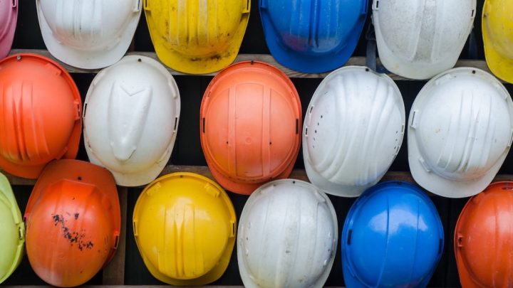 Colorful construction helmets in orange, yellow, white, and blue neatly lined up on a wall, emphasizing safety on the connected jobsite.