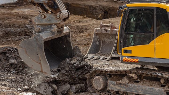 A yellow excavator digs and moves dirt at a construction site as operators track its progress using construction equipment tracking.