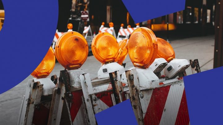 Construction barricades with orange lights line up, symbolizing barriers; blue shapes at corners suggest a connected jobsite.