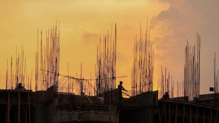Silhouette of a construction site at sunset with workers and steel rods, highlighting construction progress on a connected jobsite.