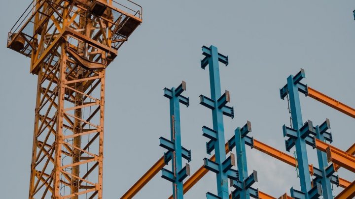 A construction crane beside a steel framework with blue and orange beams under a clear sky, representing a connected jobsite.