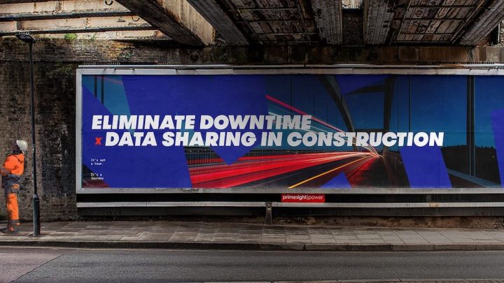 A construction worker in orange stands by a blue billboard under a bridge about data sharing to reduce downtime in construction.