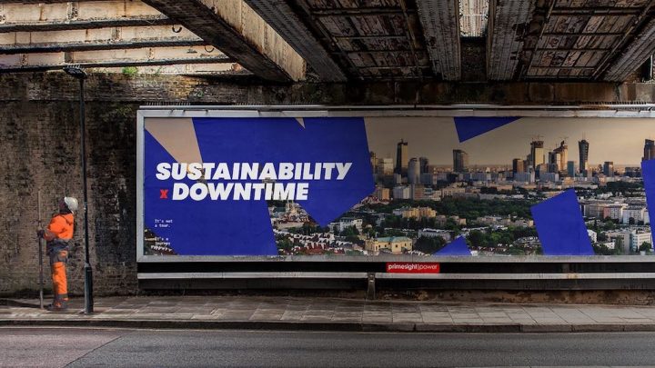 Worker in orange stands under a bridge by a "SUSTAINABILITY x DOWNTIME" billboard, suggesting connected jobsite themes.