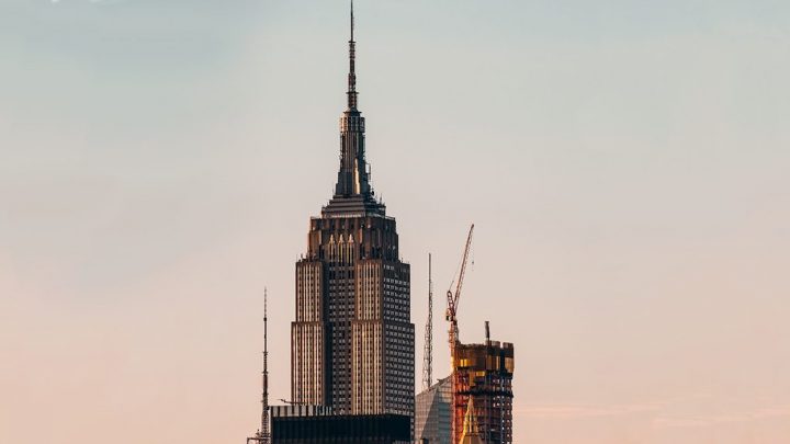 Empire State Building and a nearby skyscraper under construction with cranes, highlighting New York’s skyline and connected jobsite.