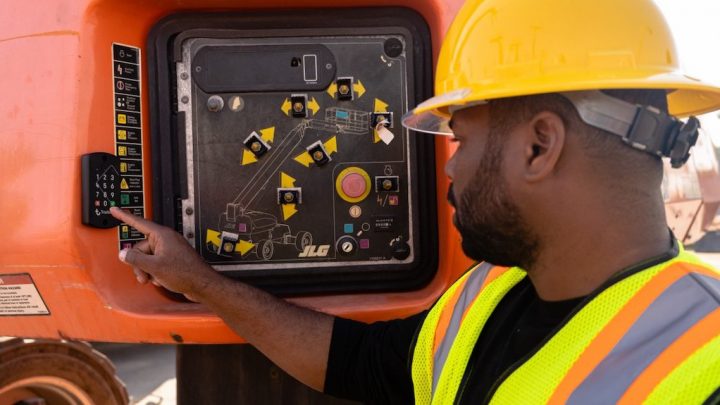 A construction worker in a yellow hard hat uses a telematics control panel on heavy machinery at a connected jobsite.