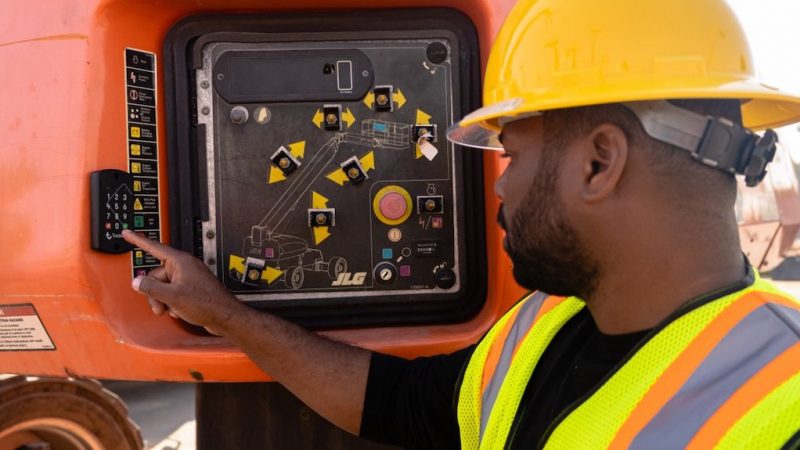 A construction worker in a yellow hard hat uses a telematics control panel on heavy machinery at a connected jobsite.