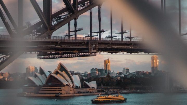 Sydney Opera House and skyline framed by Harbour Bridge, yellow ferry on water at sunset—city energized by 5G for connected jobsite.