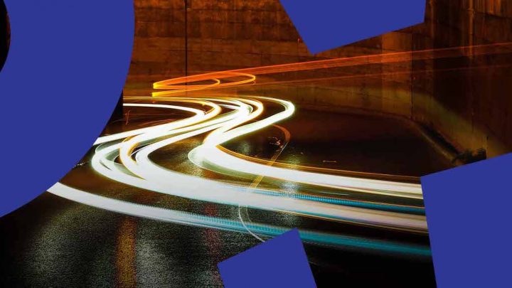 Nighttime long-exposure of a road with vehicle light trails and blue geometric overlays, evoking connected jobsite technology.