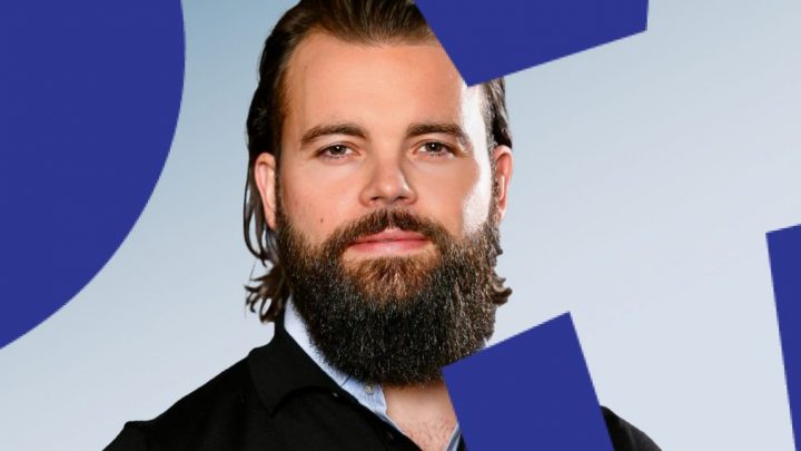 A bearded man in a dark shirt looks at the camera, with blue geometric shapes suggesting a modern construction IoT setting.