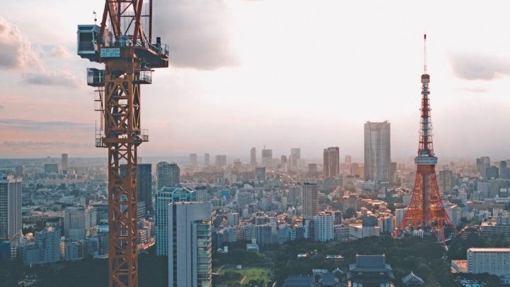 A sunset cityscape with a tall orange crane on the left and Tokyo Tower on the right, highlighting construction equipment tracking.