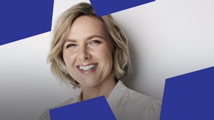 A smiling woman with short blonde hair stands against a light background, framed by blue shapes—highlighting construction IoT themes.