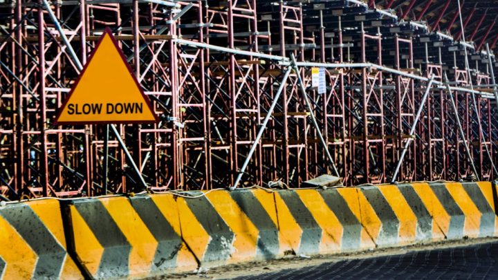 A yellow SLOW DOWN sign and striped barrier stand before scaffolding at an active construction zone, highlighting a connected jobsite.