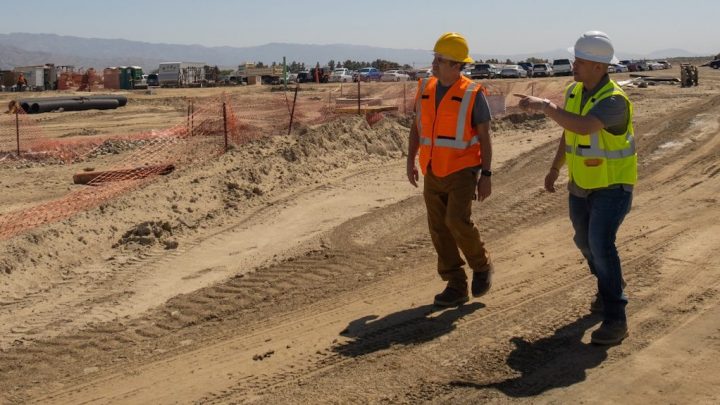 Two construction workers walk and talk at a large site, while a fleet manager oversees equipment and vehicles for fleet management.