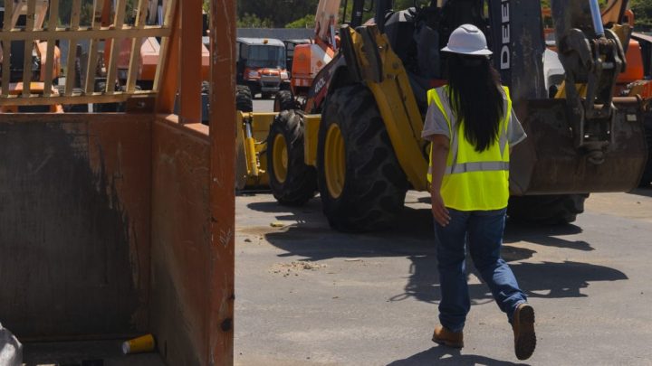 A construction worker in safety gear walks toward telematics-enabled machinery at a busy construction site, highlighting connected jobsite.