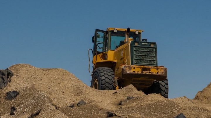 A yellow bulldozer on a dirt mound under a blue sky, door open and large tires visible—used for construction equipment tracking.