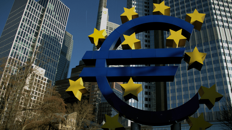 Large blue euro symbol with yellow stars in front of modern skyscrapers, illustrating EU funding’s impact on construction and connected jobsites in Central and Eastern Europe, under a clear sky with trees at the bottom left.