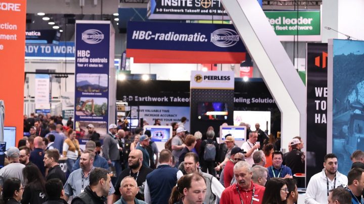 A large crowd at a busy trade show explores colorful booths and banners, networking and learning about construction IoT solutions.