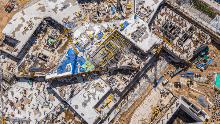 Aerial view of a large construction site with concrete structures, scattered materials, workers, and equipment using telematics.