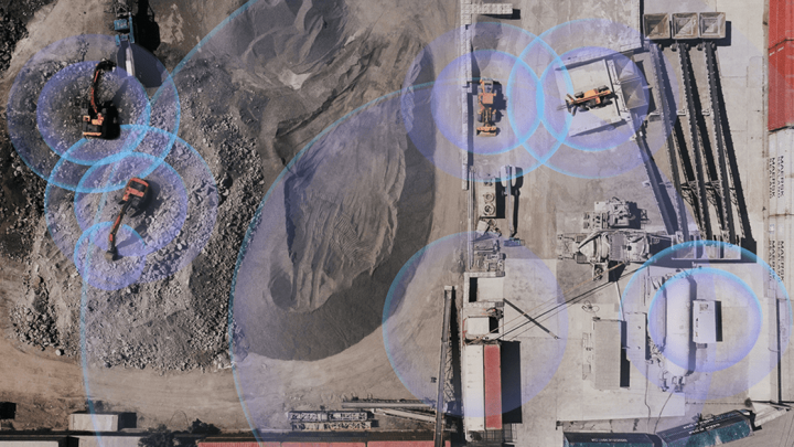 Aerial view of a construction site with vehicles and equipment, blue overlays showing connected jobsite technology across dirt and gravel.