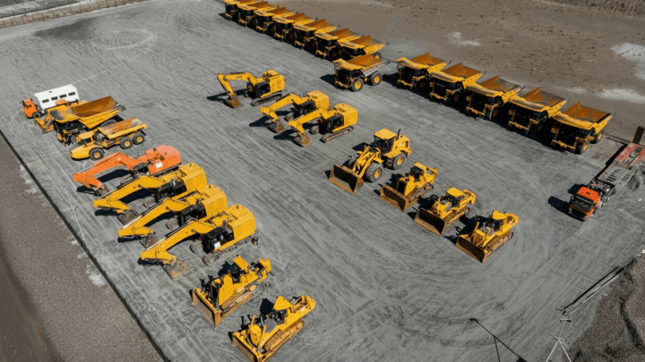 Aerial view of a construction equipment lot with yellow machines and trucks parked in rows, highlighting fleet management.