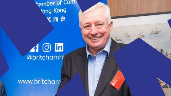 A smiling man in a suit stands before a blue tech-themed banner; dark shapes and a painting with ships hint at fleet management.