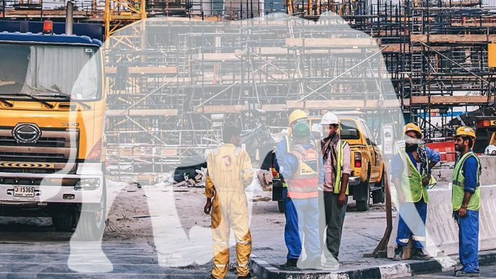 Construction workers in safety gear discuss minimizing downtime near a yellow truck at a busy site, highlighting construction IoT.