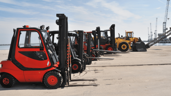 Red forklifts and a yellow wheel loader parked at an industrial port, with cranes and containers, illustrating fleet management.