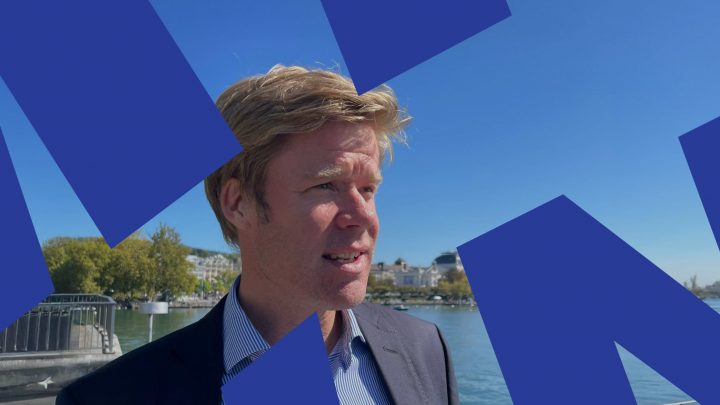 A man in a suit stands by the waterfront on a sunny day, with tech-inspired blue shapes hinting at construction IoT.