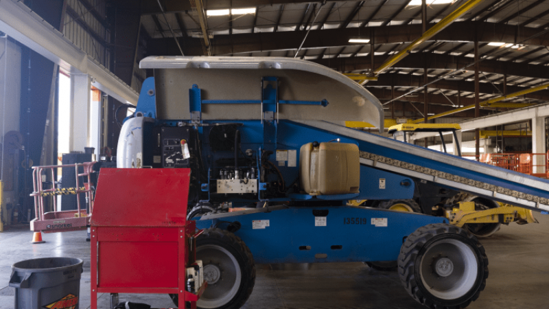 A blue and white industrial machine with a conveyor belt sits in a warehouse among tools, equipment, and fleet vehicles for fleet management.