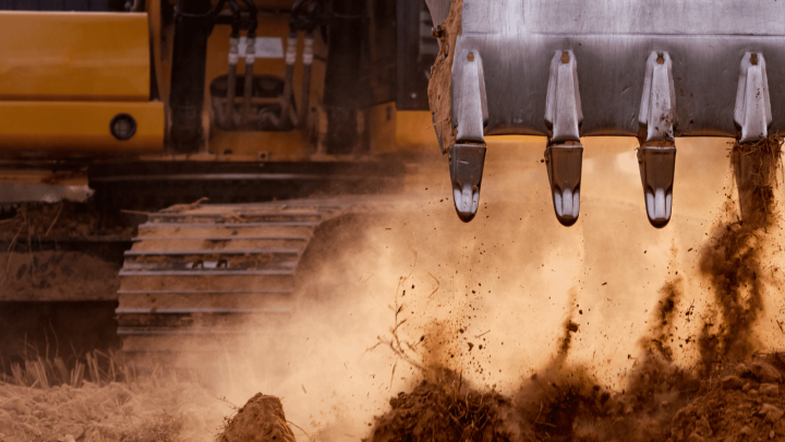 Close-up of an excavator bucket digging into the ground, dirt flying, with metal tracks behind—showing construction IoT in action.