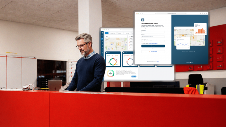 A man with glasses at a red desk uses a laptop, with construction analytics dashboards overlaid; office has shelves and red accents.