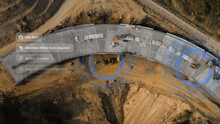 Aerial view of a curved bridge under construction with vehicles and workers, showing a connected jobsite and alert icons on the left.