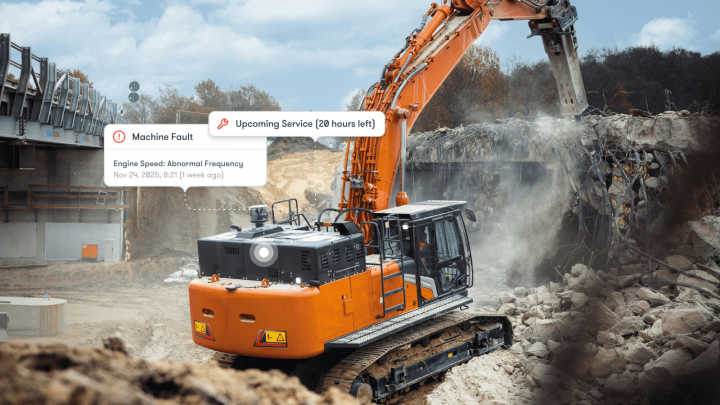 An orange excavator demolishes concrete at a construction site, with on-screen alerts for faults and service—construction telematics.