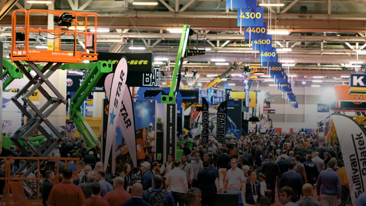 A crowd walks through bauma 2025's indoor trade show, surrounded by construction equipment and banners, highlighting connected jobsite.