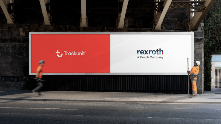 Two construction workers stand under a bridge near a billboard with Trackunit and Rexroth, a Bosch company, logos displayed.