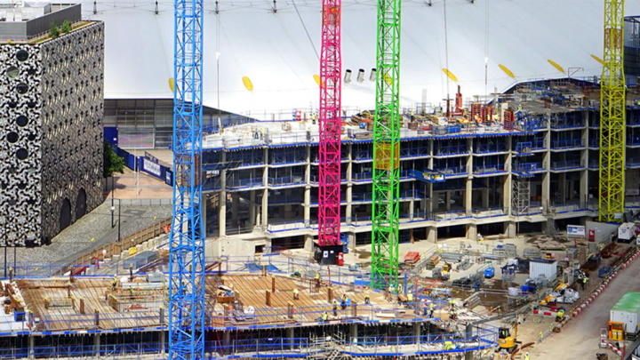Brightly colored cranes from Point of Rental at a construction site with scaffolding, materials, and a multi-story building—fleet management.
