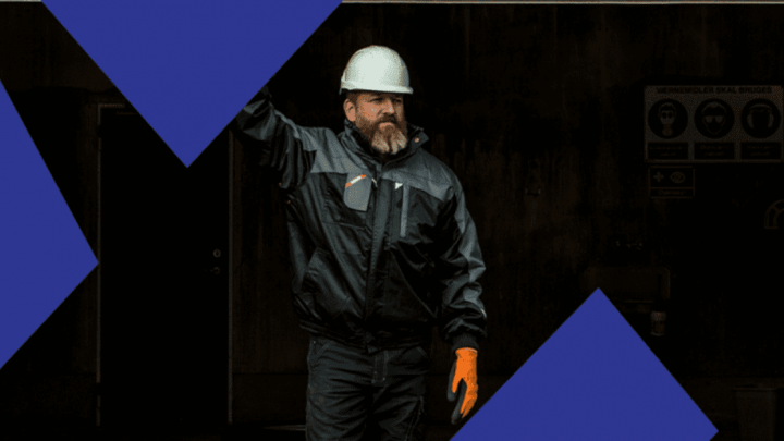 A bearded man in a white hard hat and orange gloves raises one arm, symbolizing data sharing for construction IoT, on a dark background.