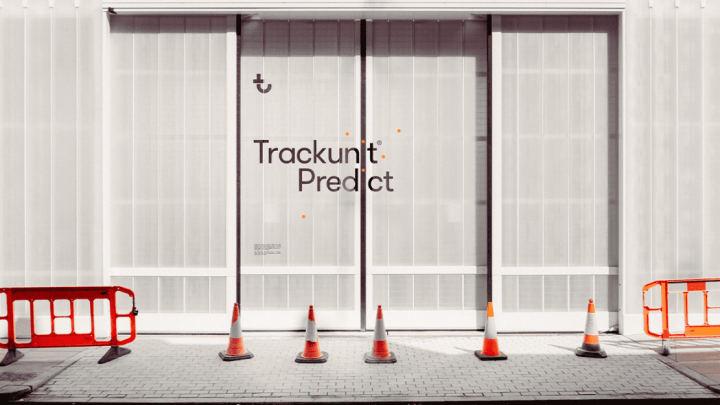 A white building labeled Trackunit Predict with glass doors, cones, and barriers, hinting at restricted access for construction IoT.