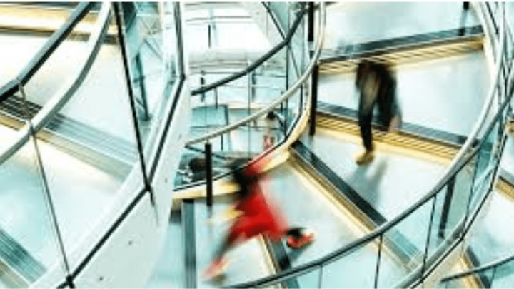 Blurred figures move on a spiral staircase with metal railings and glass panels, suggesting connected jobsite activity.