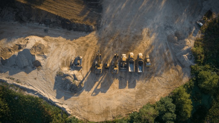 Aerial view of construction vehicles with Trackunit lined up on a dirt site, highlighting fleet management in action.