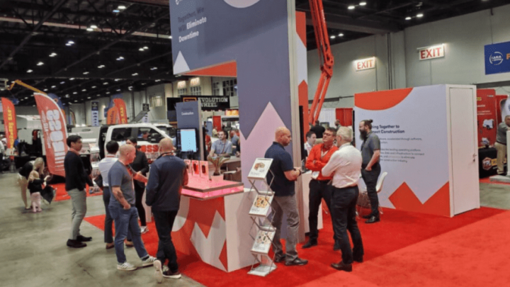 People gather at a bright Trackunit booth with red carpet at an indoor trade show, highlighting construction equipment tracking.