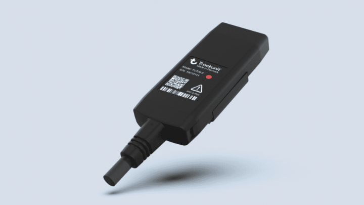 A black Trackunit GPS tracking device with a QR code, red status light, and warning symbol on a blue background for construction IoT.