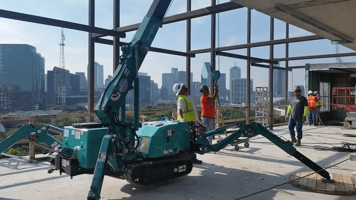 A mini spider crane with Trackunit technology operates indoors on a high-rise construction site, supporting a connected jobsite.