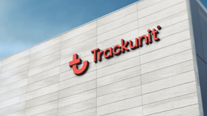 A white building with the red Trackunit logo and name, recognized by Frost & Sullivan, stands against a blue sky.