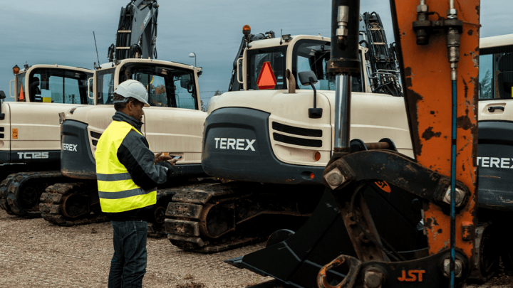 A person in a yellow vest inspects white Terex excavators at Franklin Equipment, taking notes for fleet management.