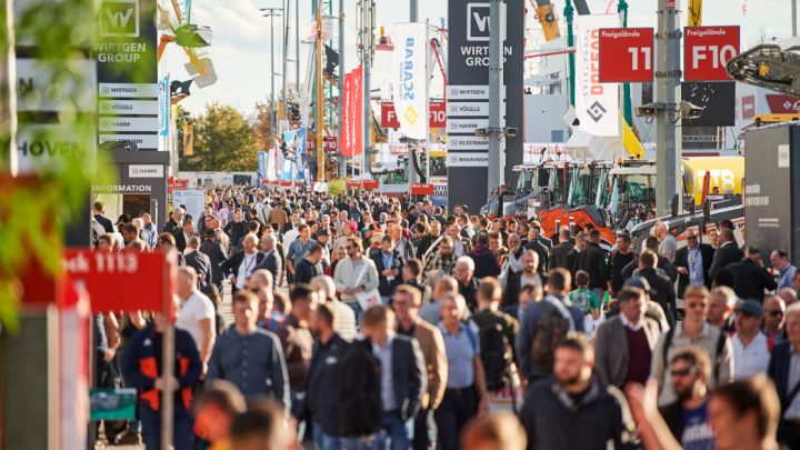 A crowd moves through an outdoor trade show with machinery, Trackunit displays, and company banners—showcasing construction IoT.