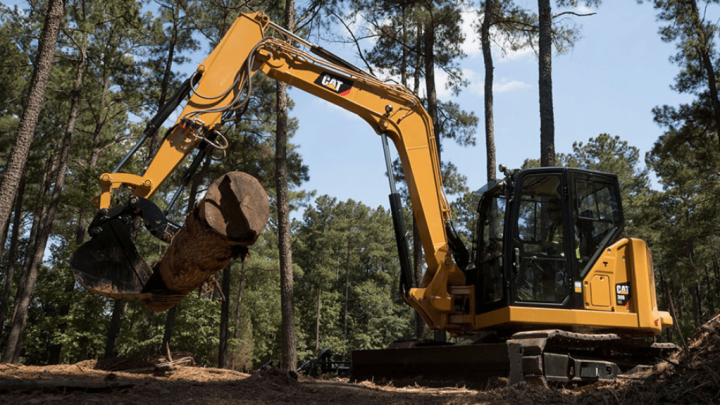 A yellow Caterpillar excavator lifts a log in a pine forest under a clear blue sky, illustrating construction equipment tracking.